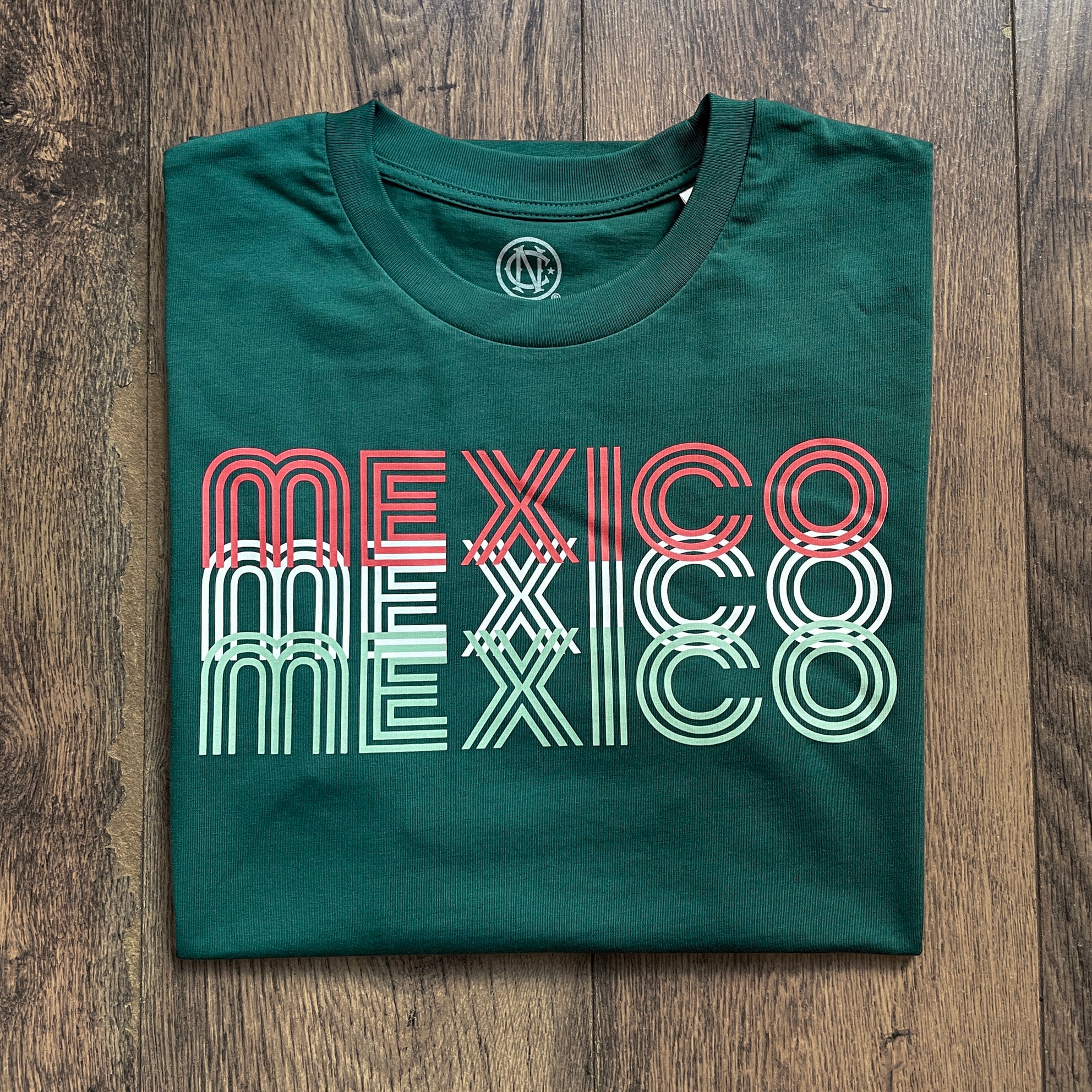 Green t-shirt with 'MEXICO' printed on it, displayed on a wooden surface.