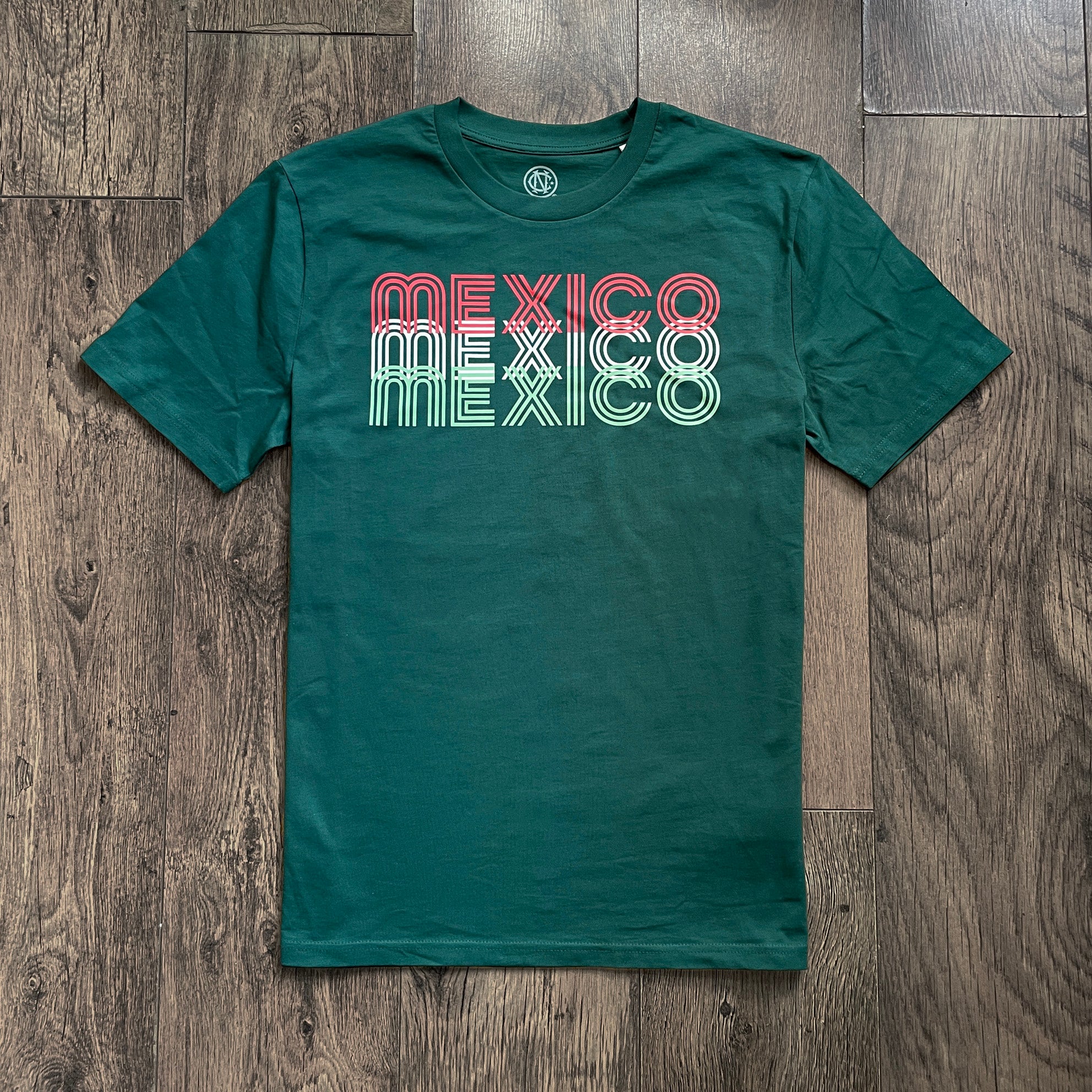 Green t-shirt with 'MEXICO' text in red, white, and green on a wooden surface